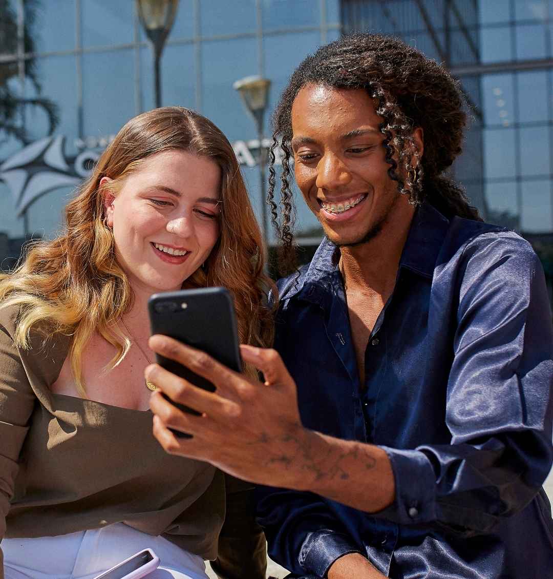 Duas pessoas sorrindo enquanto olham para um celular.