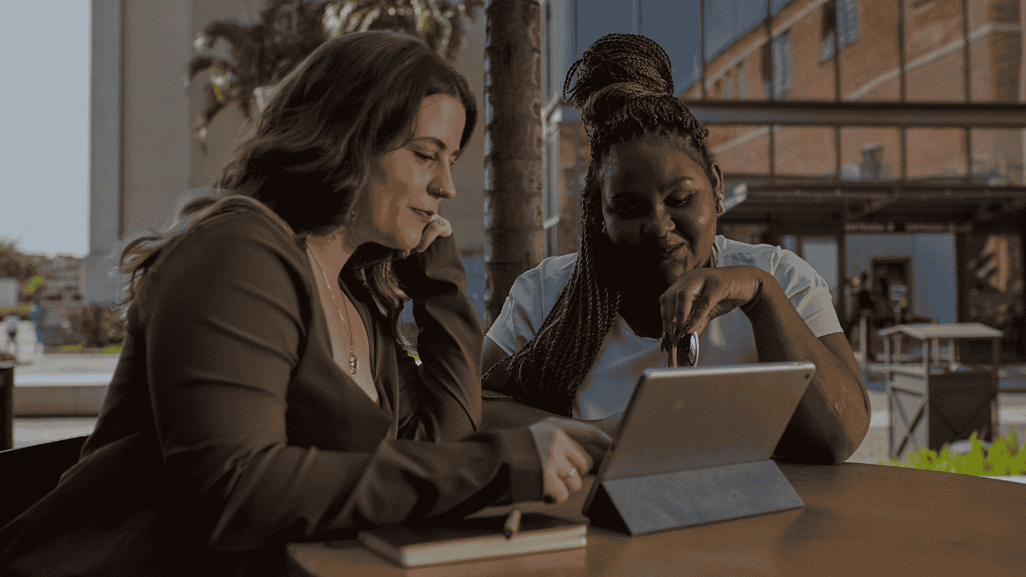 Duas mulheres colaborando em um tablet em um ambiente de trabalho.